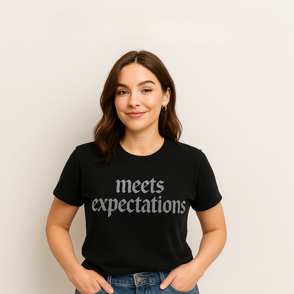 Person wearing a black t-shirt with 'meets expectations' text on a plain background