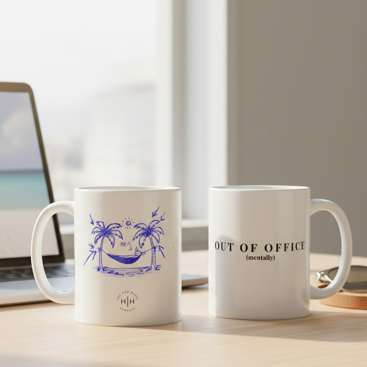 Two white mugs with blue and black text and graphics on a desk with a laptop.